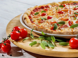 eine Pizza auf einen Holzbrett mit Tomaten angerichtet